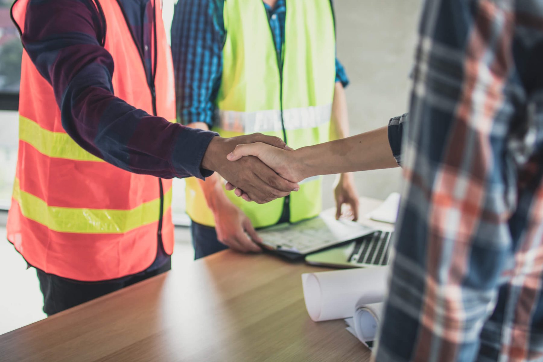 two workers shaking hands with another worker standing by